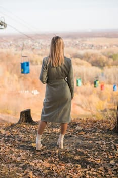 Back view blonde woman in elegant gray coat walks in the sunny autumn season park. Generation z and gen z youth concept.