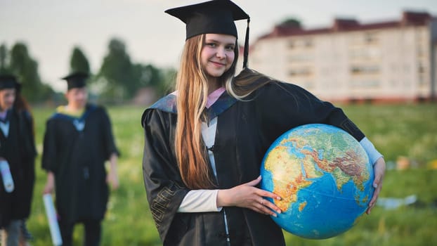Graduate student girl poses with a globe in a meadow.