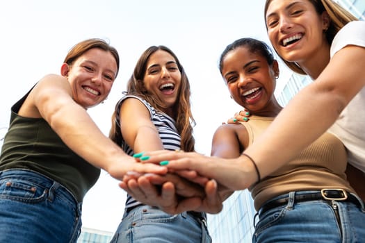 Low angle view of multiracial female friends stacking hands in unity and support looking at camera.