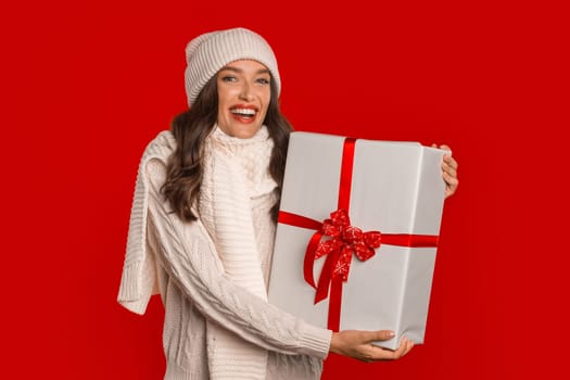 lady wearing Santa hat holds wrapped present box, red background
