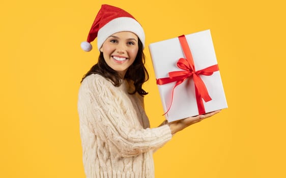 Happy lady holds New Year present with bow, yellow backdrop