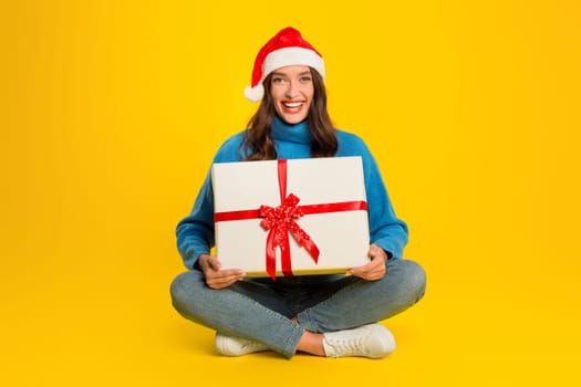 woman sitting with wrapped present box on yellow studio background