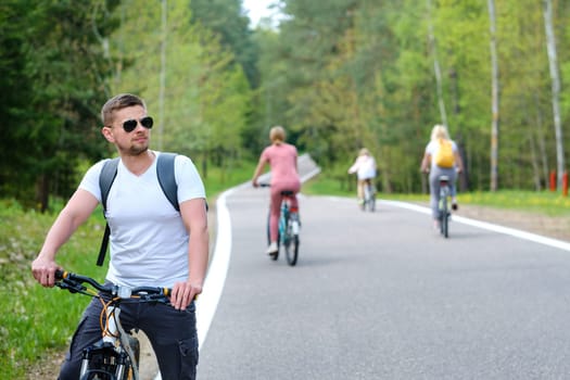 A group of cyclists with backpacks ride bicycles on a forest road enjoying nature