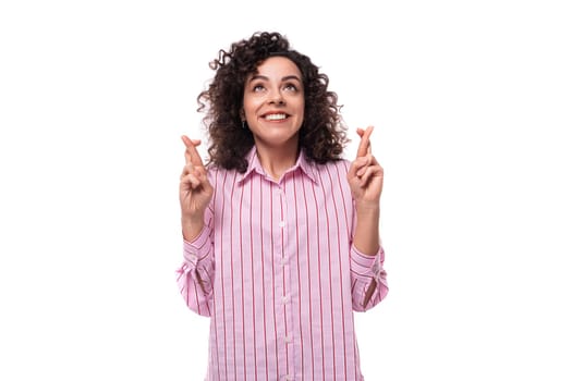 young creative woman with a curly hairstyle in a striped pink blouse crossed her fingers in anticipation of a miracle