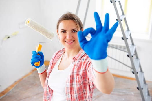 Young smiling woman with roller brush showing ok gesture, copy space