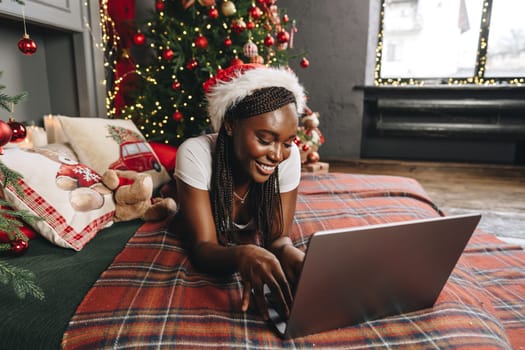 Young African woman on bed using laptop on Christmas eve