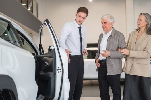 A salesman in a car dealership shows a car to a mature married couple.