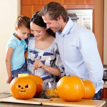Halloween, pumpkin and a family in the kitchen of their house together for holiday celebration. Creative, smile or happy with a mom, dad and daughter carving a face into a vegetable for decoration.