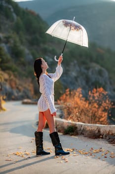 woman umbrella leaves , She holds him over her head, autumn leaves are falling out of him. Beautiful woman in a dress with an umbrella in the autumn park on the road in the mountains