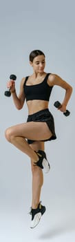 Fitness woman wearing sportswear doing cardio exercises with dumbbells on studio background