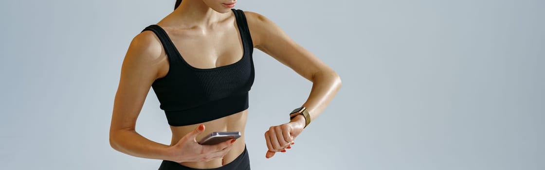 Athletic woman checking her smartwatch after training over studio background