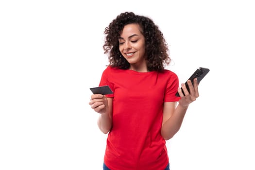 young pretty curly brunette woman dressed in a red basic t-shirt enjoys online payments. e-business concept