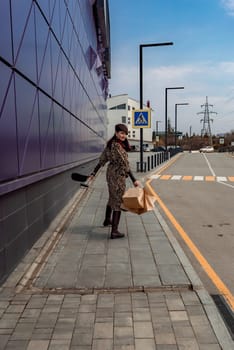 A happy shopaholic girl keeps her bags near the shopping center. A woman near the store is happy with her purchases, holding bags. Dressed in a leopard print dress. Consumer concept.