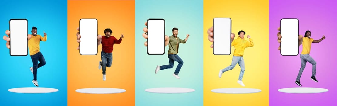 Positive excited young diverse men show big smartphone with empty screen, jump at platform