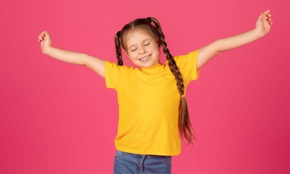 Carefree young girl with arms stretched out wide posing over pink background