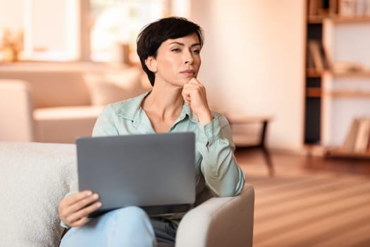 Pensive middle aged lady browsing on her laptop at home