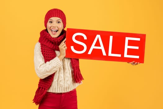 woman in winter clothes holding Sale sign on yellow backdrop