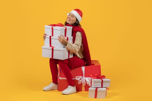 woman holding stack of wrapped Christmas packages on yellow backdrop