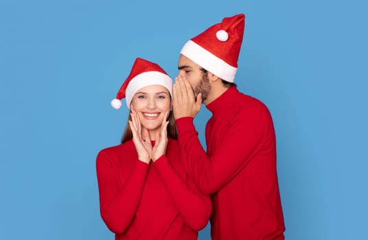 Secret Santa. Man Wearing Xmas Hat Whispering To His Excited Girlfriend's Ear
