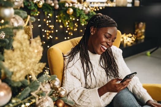 Young beautiful African woman using her phone at home decorated for Christmas season