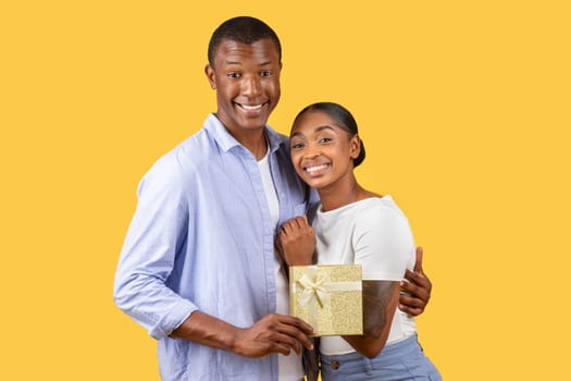 Happy Black couple, man with gift, embrace lady on yellow background