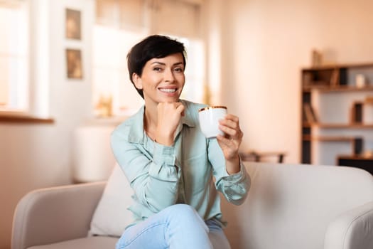 Middle aged woman enjoying hot tea sitting on sofa indoor