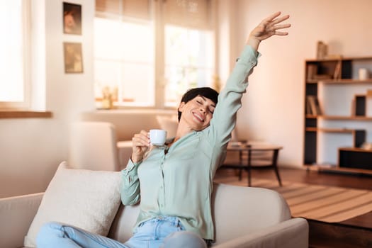 Relaxed woman holding coffee cup stretching in living room