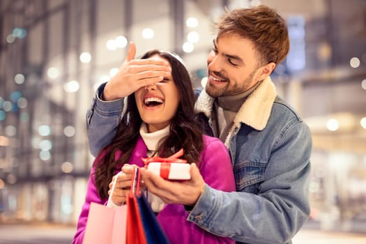man covering woman's eyes for surprise gift shopping at mall