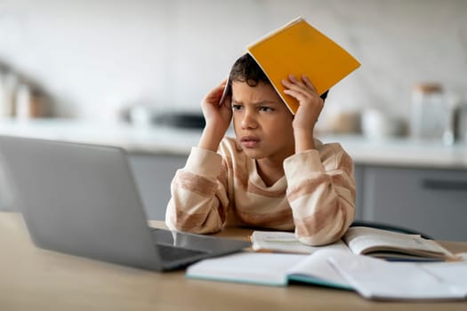 Stressed Black Boy Using Laptop And Covering Head With Workbook At Home