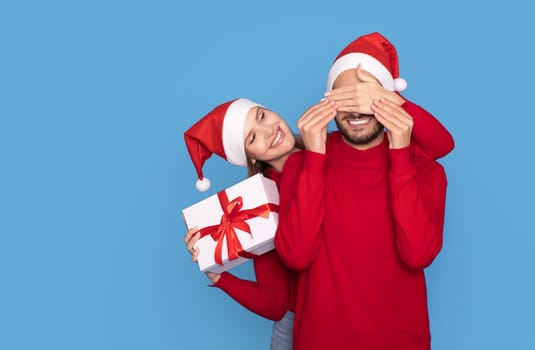 Merry Christmas. Young Woman Surprising Boyfriend With Xmas Gift, Covering His Eyes