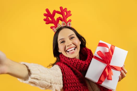 lady holding New Year present making selfie on yellow backdrop