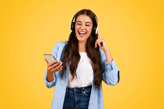 Happy teenager student woman typing on smartphone with headphones, sing song