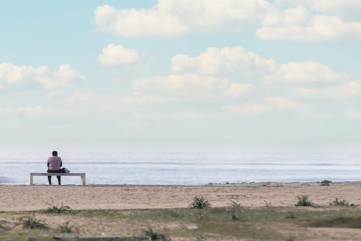 A Tranquil Moment: A Person Sitting on a Bench, Enjoying the Serene Beachscape