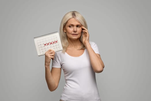 Stressed Mature Woman Looking At Her Menstrual Calendar With Crossed Out Dates