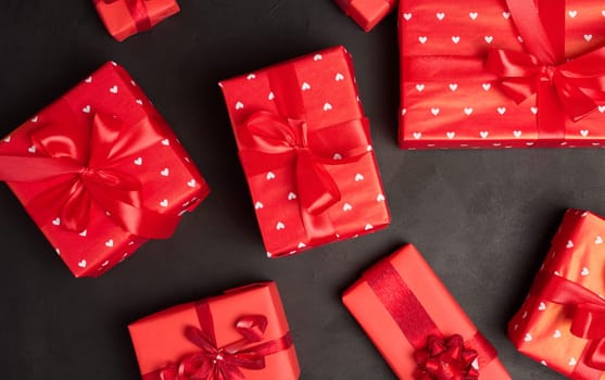 Boxes packed in red paper and tied with ribbon on a black background, gifts. 