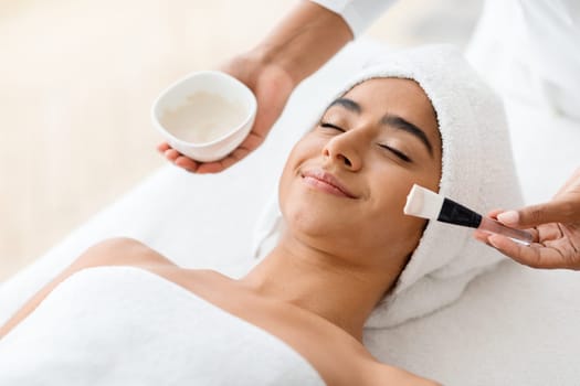 Woman getting facial nourishing mask by professional beautician at spa