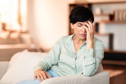 Middle aged lady clutching head in pain on couch indoor