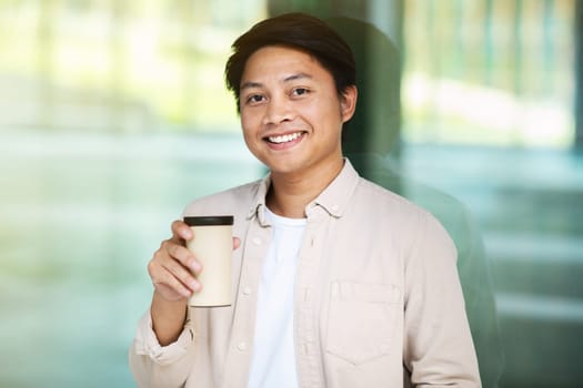 Portrait of cheerful millennial asian man drinking coffee at downtown