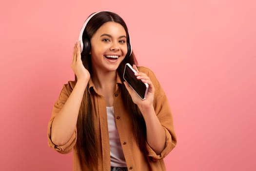 Cheerful teen girl listening music in wireless headphones and singing