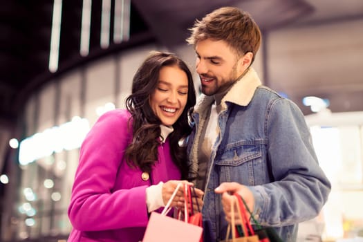 shopaholics couple embracing standing with shopping bags, enjoying winter evening