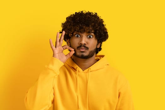 Handsome indian guy zipping his mouth on yellow background