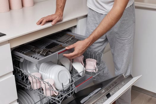 close-up, man loads dishes into the dishwasher in the kitchen