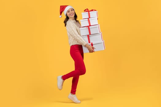 Happy lady posing with stack of Christmas presents, yellow backdrop