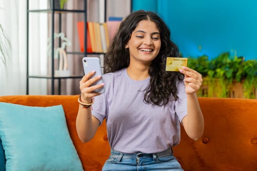 Indian woman using credit bank card, smartphone transferring money purchases online shopping