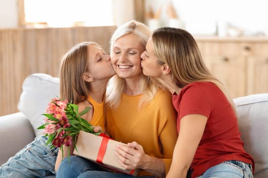 Adoring adult daughter and her young granddaughter kissing their grandmother