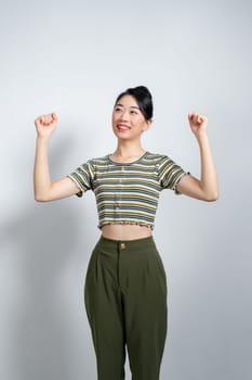 Beautiful Asian woman raises arms and fists clenched with celebrating victory expressing success.