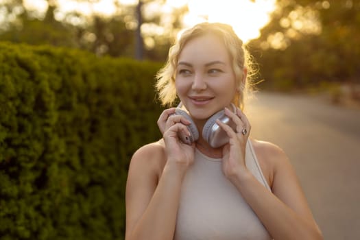 Portrait of fit girl preparing for running in workout clothes looking at camera smiling. Beautiful happy sportswoman enjoying doing sports listening to music using headphones. Music concept.