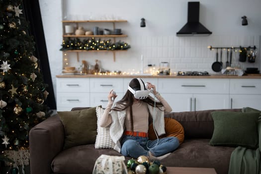 A stylish young woman in a cozy Christmas atmosphere at home, wearing a virtual reality headset.