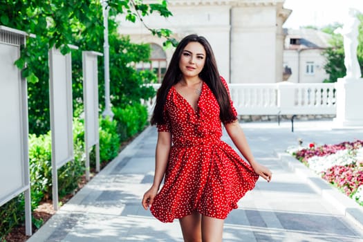 Beautiful brunette woman in red polka dot dress walks the streets of the city