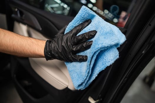 A man wipes the surface of the car interior with a microfiber cloth.